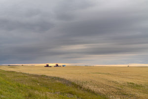 Red harvest combines near the horizon under layered storm clouds