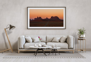 Desert highway crossing a broad plain toward silhouetted rock formations