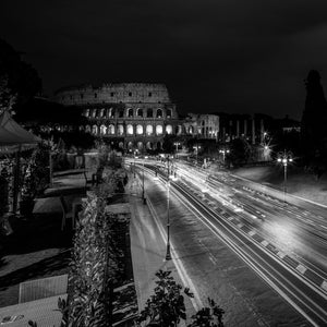Night photograph of Rome’s Colosseum with light trails along a curving road
