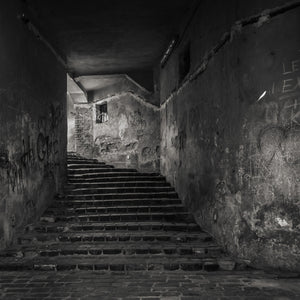 Black and white photograph of an old stairwell with graffiti-covered plaster