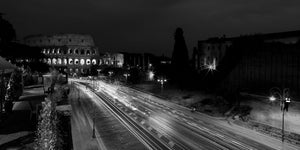 Black and white panorama of light trails leading toward the illuminated Colosseum