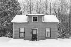Black and white winter photograph of an old rural house beneath snowy trees