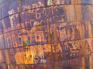Colour industrial abstract of orange corrosion and worn lettering on curved metal