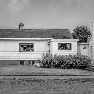 Small house with crowded window displays and shrubs beside a lawn