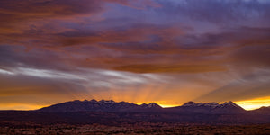 Sierra Mountains at sunset beneath layered purple clouds and a golden horizon.