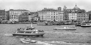 Passenger boats and motorboats leave wakes along a Venetian waterfront
