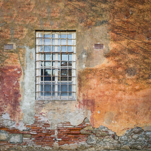 White window behind rusty bars in a peeling Italian facade