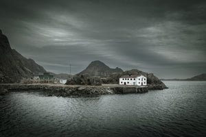 Old white Norwegian building on a rocky harbour shore