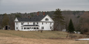 Large white rural house with dark roof and red brick chimneys in Maine