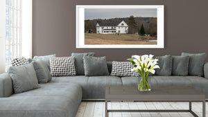 Panoramic photograph of a white house among bare trees and evergreens