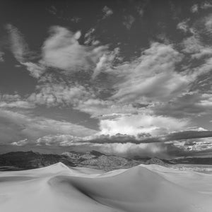 Monochrome desert landscape with pale dunes and a towering cloud filled sky
