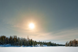 Bright sun and pale blue sky over a snow covered Ontario lake