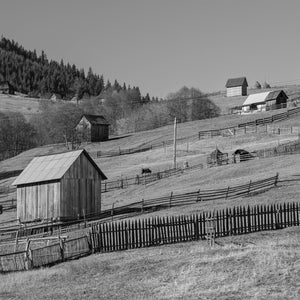 Monochrome Romanian farmland with barns scattered across a grassy hill